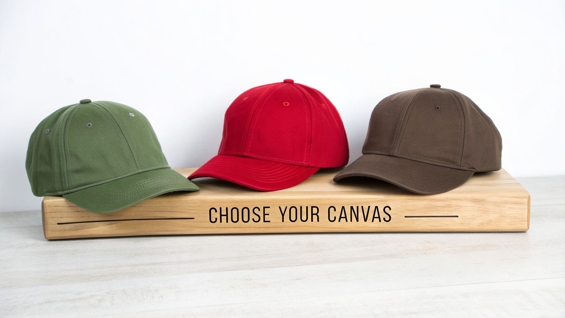 Three blank baseball caps in green, red, and brown on a wooden block, ready for customization.