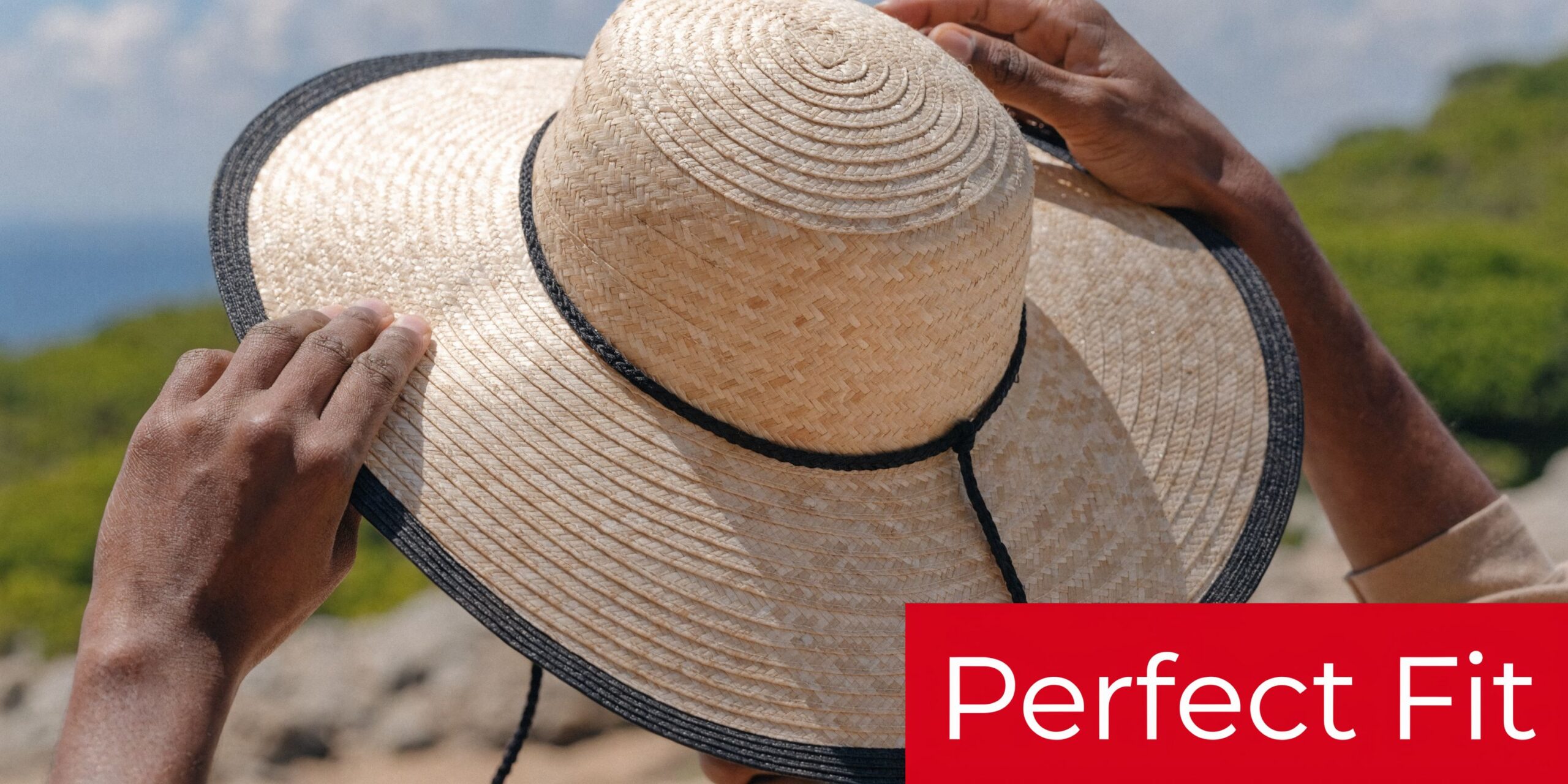 A person adjusting a wide-brimmed straw hat with a black trim on a sunny day outdoors.