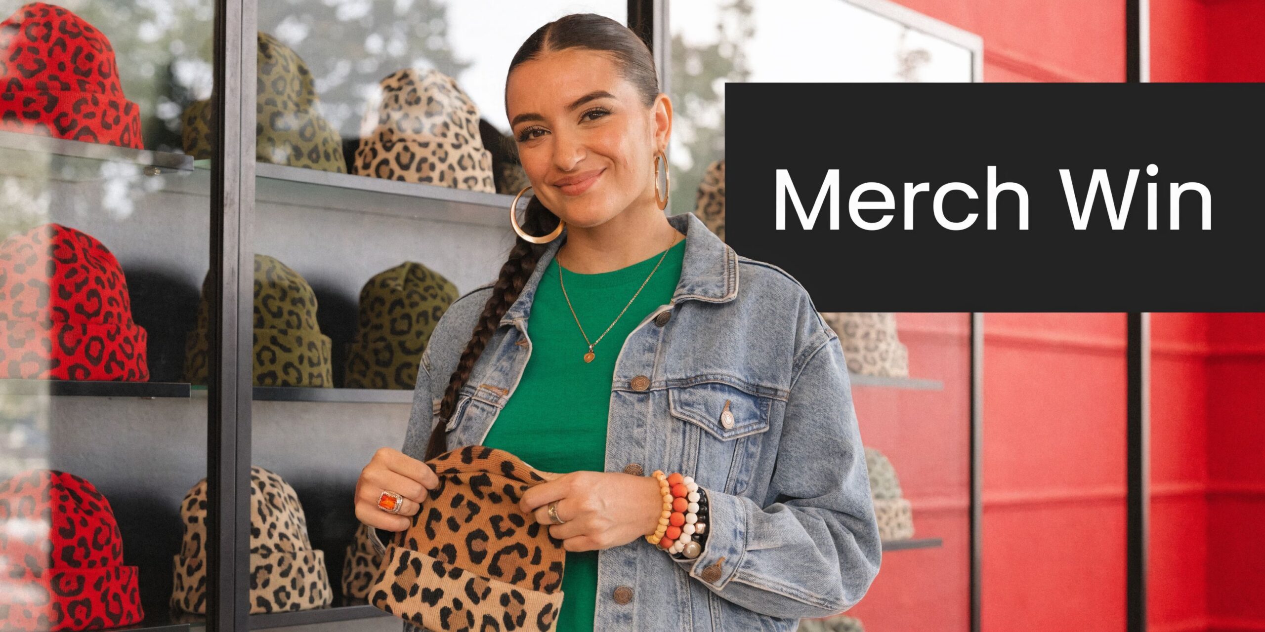 A smiling woman holding a leopard print beanie in front of a store shelf display.