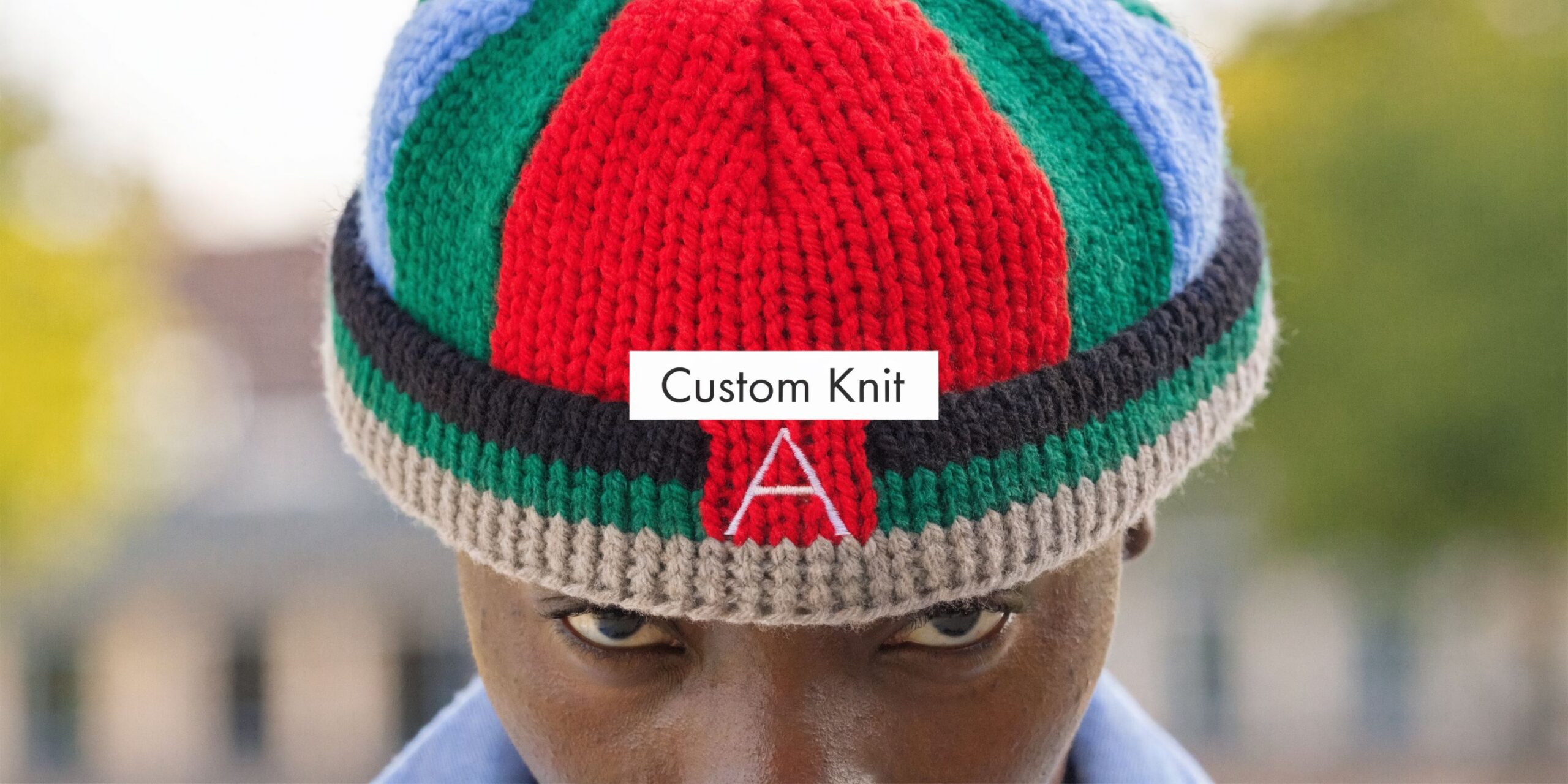 A close-up of a person wearing a colorful multi-striped knit stocking cap with a prominent white letter A.