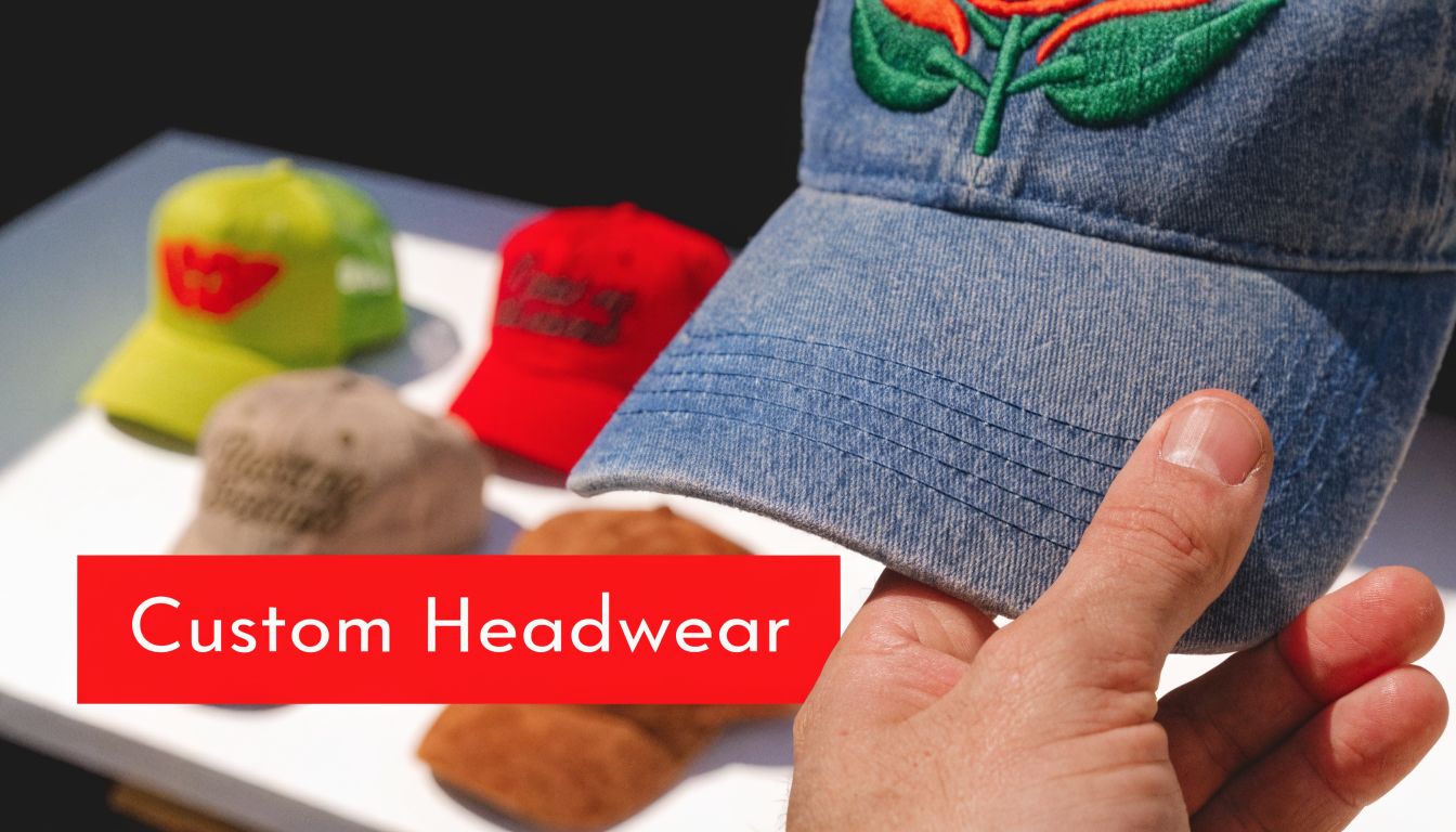 A hand holding a blue denim baseball cap with various colorful embroidered hats on a table.
