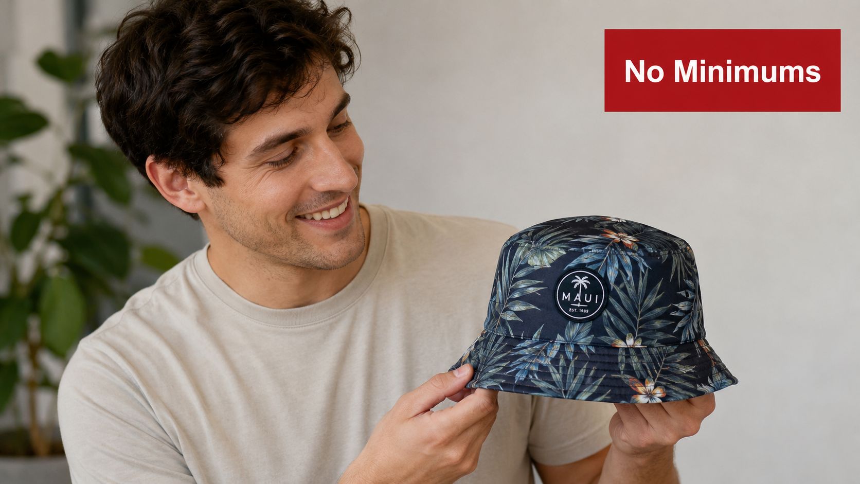 A smiling young man holding a stylish custom-branded floral print bucket hat in a bright studio.