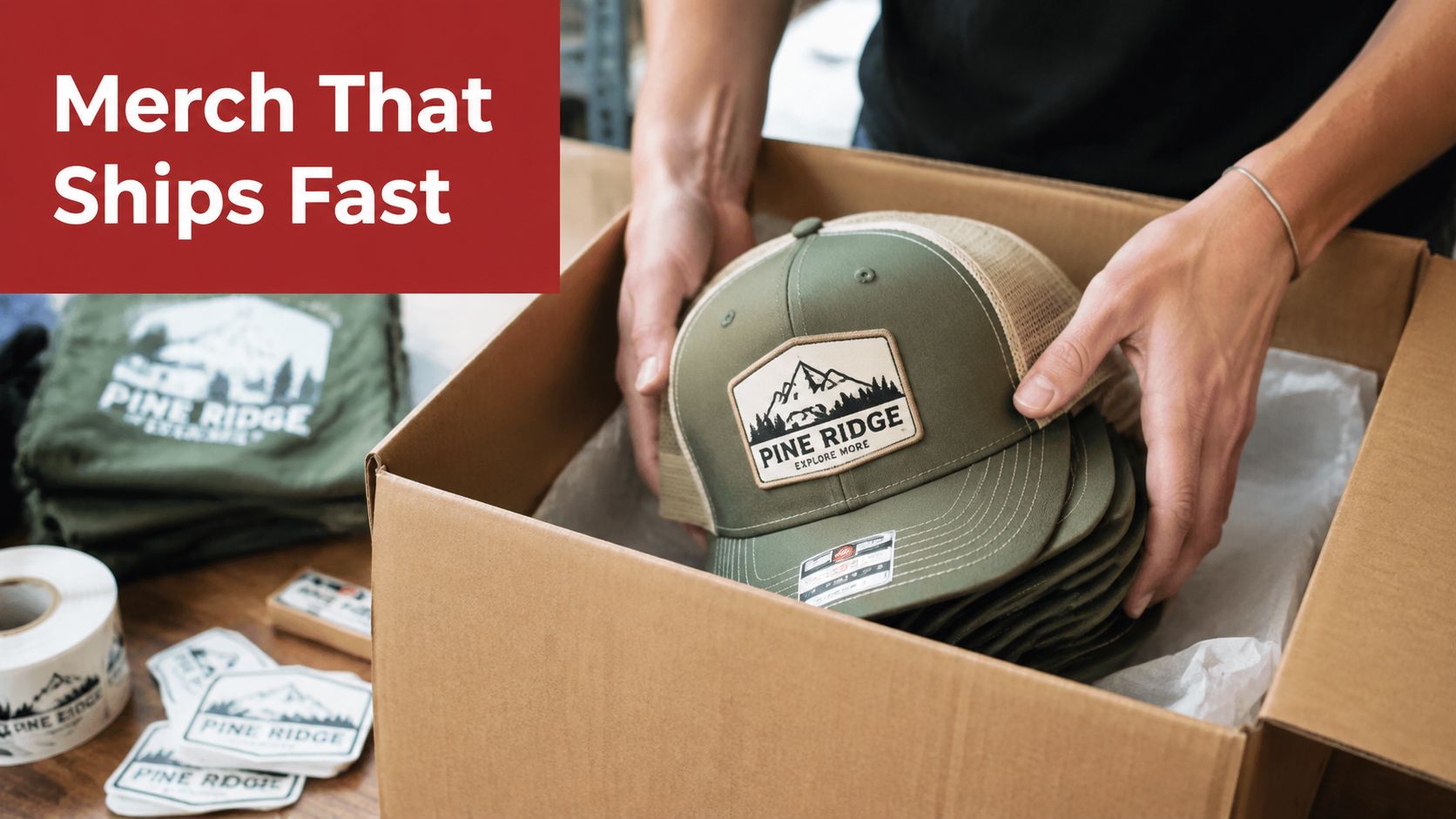 A person carefully packing several green mesh trucker hats with Pine Ridge branding into a shipping box.